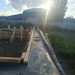 Строительство дома «Пётр» 54 м² в Каскелене, 2026: залитая бетоном лента фундамента в деревянной опалубке, на фоне предгорья Заилийского Алатау