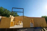 Строительство цеха «Евгений» 400 м² в мкр Шанырак (Алматы), 2026: стены цеха собраны по периметру плиты, в проёме установлен стальной портал ворот, внутри сложен запас СИП-панелей
