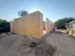 Дом «Марк» 130 м², пос. Алатау, 2026: смонтирована наружная стена из СИП-панелей на ленте фундамента, продольный вид