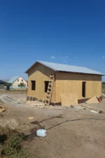 Дом «Пётр» 54 м², Каскелен, 2026: на собранной коробке из СИП-панелей смонтирована двускатная кровля из металлочерепицы с подшитыми свесами, оставлены проёмы под окна и входную дверь