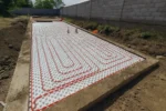 Дом «Сатурин» 165 м², Алматы, 2026: узкая захватка вдоль забора закрыта матами с бобышками, труба тёплого пола уложена спиралью от края к центру