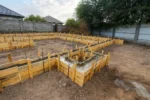Дом «Сатурин» 165 м², Алматы, 2026: в опалубку ленточного фундамента уложен бетон — часть лент и внутренний контур уже залиты, из них выпущены вертикальные стержни арматуры