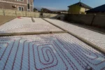 Дом «Сатурин» 165 м², Алматы, 2026: по залитым лентам фундамента разложены маты с бобышками, в них уложены контуры водяного тёплого пола из красной трубы, захватки разделены бетонными рёбрами