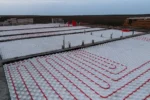 Общежитие «Доссан» 550 м², Астана, 2026: по плите разложены белые маты с бобышками, в них уложены контуры тёплого пола из красной трубы, между блоками — разделительные рейки и выпуски арматуры