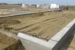 Дом «Евгений» 198 м², Лисаковск, 2026: на участке сложены пачки СИП-панелей домокомплекта, внутри контура фундамента песок разровнен техникой