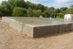 Дом «Надежда» 100 м², Павлодар, 2026: фундамент залит, поверх наполнения выведена ровная бетонная стяжка по всему пятну застройки, по краю видна фактура опалубочной доски