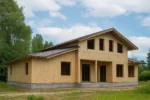Дом «А-404», 404 м², 1,5 этажа, в черновой отделке: коробка из СИП-панелей OSB-3, двускатная кровля из металлочерепицы, проёмы без окон и дверей, в проёмах видны сосновые балки перекрытия