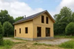 Дом «А-85Г», 85 м², 1.5 этажа, в черновой отделке: коробка из СИП-панелей OSB-3, двускатная кровля из металлочерепицы, проёмы без окон и дверей, в проёмах видны сосновые балки перекрытия