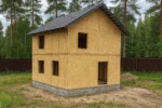 Дом «А-99», 99 м², 2 этажа, в черновой отделке: коробка из СИП-панелей OSB-3, двускатная кровля из металлочерепицы, проёмы без окон и дверей, в проёмах видны сосновые балки перекрытия