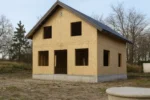 Дом «Б-187Б», 187 м², 1.5 этажа, в черновой отделке: коробка из СИП-панелей OSB-3, двускатная кровля из металлочерепицы, проёмы без окон и дверей, в проёмах видны сосновые балки перекрытия