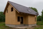 Дом «Д-107Б», 107 м², 1.5 этажа, в черновой отделке: коробка из СИП-панелей OSB-3, двускатная кровля из металлочерепицы, проёмы без окон и дверей, в проёмах видны сосновые балки перекрытия