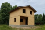Дом «Д-126», 126 м², 1.5 этажа, в черновой отделке: коробка из СИП-панелей OSB-3, двускатная кровля из металлочерепицы, проёмы без окон и дверей, в проёмах видны сосновые балки перекрытия