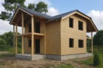 Дом «Д-172Б», 172 м², 1.5 этажа, в черновой отделке: коробка из СИП-панелей OSB-3, двускатная кровля из металлочерепицы, проёмы без окон и дверей, в проёмах видны сосновые балки перекрытия