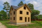 Дом «Д-180Б», 180 м², 2 этажа, в черновой отделке: коробка из СИП-панелей OSB-3, двускатная кровля из металлочерепицы, проёмы без окон и дверей, в проёмах видны сосновые балки перекрытия