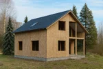 Дом «Ф-180», 180 м², 1.5 этажа, в черновой отделке: коробка из СИП-панелей OSB-3, двускатная кровля из металлочерепицы, проёмы без окон и дверей, в проёмах видны сосновые балки перекрытия