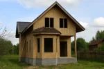 Дом «Ф-206», 206 м², 1.5 этажа, в черновой отделке: коробка из СИП-панелей OSB-3, двускатная кровля из металлочерепицы, проёмы без окон и дверей, в проёмах видны сосновые балки перекрытия