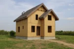 Дом «Г-104», 104 м², 1.5 этажа, в черновой отделке: коробка из СИП-панелей OSB-3, двускатная кровля из металлочерепицы, проёмы без окон и дверей, в проёмах видны сосновые балки перекрытия