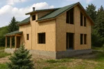 Дом «Х-180», 180 м², 1.5 этажа, в черновой отделке: коробка из СИП-панелей OSB-3, двускатная кровля из металлочерепицы, проёмы без окон и дверей, в проёмах видны сосновые балки перекрытия