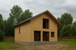 Дом «И-189Б», 189 м², 1.5 этажа, в черновой отделке: коробка из СИП-панелей OSB-3, двускатная кровля из металлочерепицы, проёмы без окон и дверей, в проёмах видны сосновые балки перекрытия