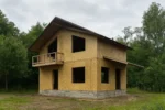 Дом «К-108В», 108 м², 1.5 этажа, в черновой отделке: коробка из СИП-панелей OSB-3, двускатная кровля из металлочерепицы, проёмы без окон и дверей, в проёмах видны сосновые балки перекрытия
