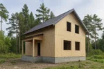 Дом «К-118В», 118 м², 1.5 этажа, в черновой отделке: коробка из СИП-панелей OSB-3, двускатная кровля из металлочерепицы, проёмы без окон и дверей, в проёмах видны сосновые балки перекрытия