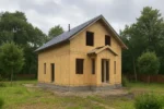 Дом «К-127», 127 м², 1.5 этажа, в черновой отделке: коробка из СИП-панелей OSB-3, двускатная кровля из металлочерепицы, проёмы без окон и дверей, в проёмах видны сосновые балки перекрытия