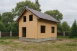 Дом «Н-104Б», 104 м², 1.5 этажа, в черновой отделке: коробка из СИП-панелей OSB-3, двускатная кровля из металлочерепицы, проёмы без окон и дверей, в проёмах видны сосновые балки перекрытия