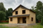 Дом «Н-104В», 104 м², 1.5 этажа, в черновой отделке: коробка из СИП-панелей OSB-3, двускатная кровля из металлочерепицы, проёмы без окон и дверей, в проёмах видны сосновые балки перекрытия