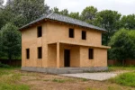 Дом «Н-151», 151 м², 2 этажа, в черновой отделке: коробка из СИП-панелей OSB-3, вальмовая кровля из металлочерепицы, проёмы без окон и дверей, в проёмах видны сосновые балки перекрытия