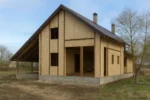 Дом «Н-194», 194 м², 1.5 этажа, в черновой отделке: коробка из СИП-панелей OSB-3, двускатная кровля из металлочерепицы, проёмы без окон и дверей, в проёмах видны сосновые балки перекрытия