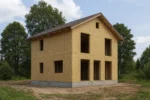 Дом «О-128», 128 м², 2 этажа, в черновой отделке: коробка из СИП-панелей OSB-3, двускатная кровля из металлочерепицы, проёмы без окон и дверей, в проёмах видны сосновые балки перекрытия