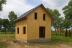 Дом «П-109Б», 109 м², 1.5 этажа, в черновой отделке: коробка из СИП-панелей OSB-3, двускатная кровля из металлочерепицы, проёмы без окон и дверей, в проёмах видны сосновые балки перекрытия