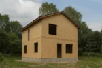 Дом «П-126Б», 126 м², 1.5 этажа, в черновой отделке: коробка из СИП-панелей OSB-3, двускатная кровля из металлочерепицы, проёмы без окон и дверей, в проёмах видны сосновые балки перекрытия