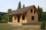 Дом «П-131Б», 131 м², 1.5 этажа, в черновой отделке: коробка из СИП-панелей OSB-3, двускатная кровля из металлочерепицы, проёмы без окон и дверей, в проёмах видны сосновые балки перекрытия