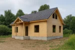 Дом «П-180», 180 м², 1.5 этажа, в черновой отделке: коробка из СИП-панелей OSB-3, двускатная кровля из металлочерепицы, проёмы без окон и дверей, в проёмах видны сосновые балки перекрытия