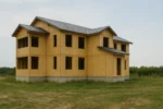 Дом «П-434», 434 м², 2 этажа, в черновой отделке: коробка из СИП-панелей OSB-3, двускатная кровля из металлочерепицы, проёмы без окон и дверей, в проёмах видны сосновые балки перекрытия