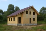 Дом «Р-171», 171 м², 1.5 этажа, в черновой отделке: коробка из СИП-панелей OSB-3, двускатная кровля из металлочерепицы, проёмы без окон и дверей, в проёмах видны сосновые балки перекрытия