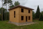 Дом «С-105», 105 м², 2 этажа, в черновой отделке: коробка из СИП-панелей OSB-3, вальмовая кровля из металлочерепицы, проёмы без окон и дверей, в проёмах видны сосновые балки перекрытия