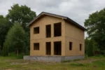 Дом «С-142В», 142 м², 2 этажа, в черновой отделке: коробка из СИП-панелей OSB-3, двускатная кровля из металлочерепицы, проёмы без окон и дверей, в проёмах видны сосновые балки перекрытия