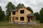 Дом «С-160В», 160 м², 2 этажа, в черновой отделке: коробка из СИП-панелей OSB-3, двускатная кровля из металлочерепицы, проёмы без окон и дверей, в проёмах видны сосновые балки перекрытия