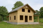 Дом «С-199В», 199 м², 1.5 этажа, в черновой отделке: коробка из СИП-панелей OSB-3, двускатная кровля из металлочерепицы, проёмы без окон и дверей, в проёмах видны сосновые балки перекрытия
