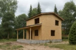 Дом «С-94В», 94 м², 2 этажа, в черновой отделке: коробка из СИП-панелей OSB-3, двускатная кровля из металлочерепицы, проёмы без окон и дверей, в проёмах видны сосновые балки перекрытия