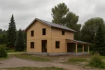 Дом «Т-153Г», 153 м², 2 этажа, в черновой отделке: коробка из СИП-панелей OSB-3, двускатная кровля из металлочерепицы, проёмы без окон и дверей, в проёмах видны сосновые балки перекрытия