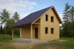 Дом «В-109В», 109 м², 1.5 этажа, в черновой отделке: коробка из СИП-панелей OSB-3, двускатная кровля из металлочерепицы, проёмы без окон и дверей, в проёмах видны сосновые балки перекрытия