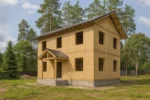 Дом «В-124», 124 м², 2 этажа, в черновой отделке: коробка из СИП-панелей OSB-3, двускатная кровля из металлочерепицы, проёмы без окон и дверей, в проёмах видны сосновые балки перекрытия