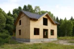 Дом «В-142В», 142 м², 1.5 этажа, в черновой отделке: коробка из СИП-панелей OSB-3, двускатная кровля из металлочерепицы, проёмы без окон и дверей, в проёмах видны сосновые балки перекрытия