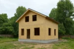 Дом «З-112», 112 м², 1.5 этажа, в черновой отделке: коробка из СИП-панелей OSB-3, двускатная кровля из металлочерепицы, проёмы без окон и дверей, в проёмах видны сосновые балки перекрытия