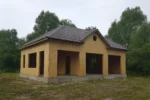 Дом «Г-143», 143 м², 1.5 этажа, в черновой отделке: коробка из СИП-панелей OSB-3, вальмовая кровля из металлочерепицы, проёмы без окон и дверей, в проёмах видны сосновые балки перекрытия