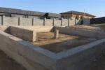 Дом «Азиза», Талгар, 2026: ленточный фундамент залит и распалублен, наружные грани лент закрыты гидроизоляционной плёнкой, внутри контура выполнена обратная засыпка грунтом