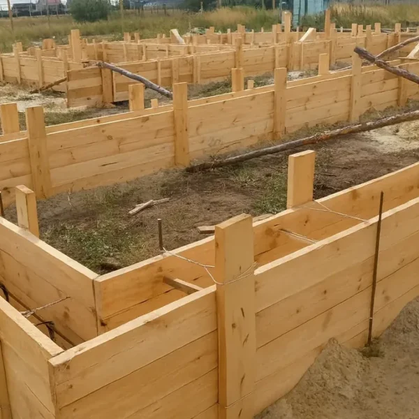 Дом «Евгений» 198 м², Лисаковск, 2026: опалубка ленточного фундамента вблизи — угол ленты со стяжками по верху щитов и выставленными вертикальными выпусками арматуры